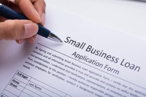 Person filling out a small business loan application form with a pen, representing the business vs personal loan process
