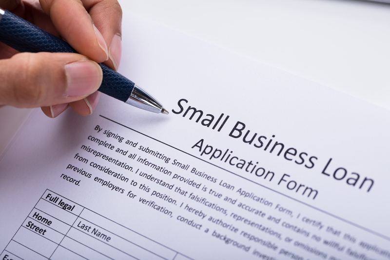 Person filling out a small business loan application form with a pen, representing the business vs personal loan process