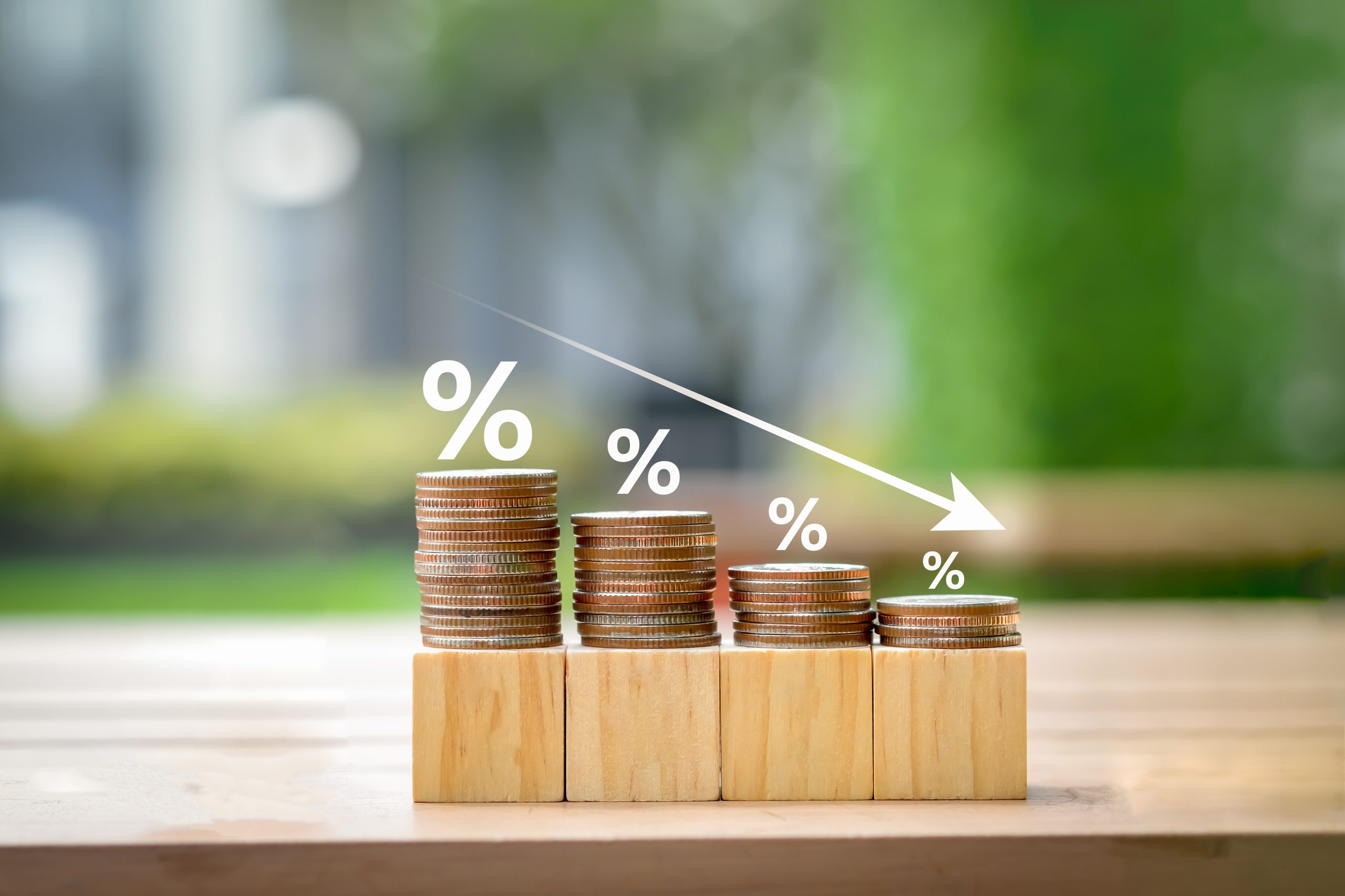 Percentage signs above descending coin stacks on wooden blocks representing the affordable interest rates of MM Credit's monthly loans